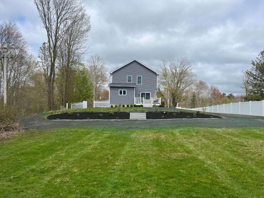Residential lawn with crisp edging and mulched beds beside a driveway in Stoughton, MA, highlighting routine upkeep and full-service lawn care.